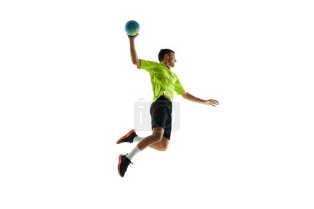 Téléchargez les photos : Image dynamique du jeune homme en uniforme, joueur de handball en mouvement pendant le jeu, s'exerçant, sautant avec une balle sur fond de studio blanc. Concept de sport professionnel, tournoi, compétition - en image libre de droit