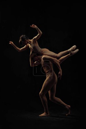 Foto de Joven hombre y mujer, bailarines de ballet haciendo creativos, hermosa actuación, bailando sobre fondo negro. Concepto de arte clásico, estética, emociones, danza de ballet, talento - Imagen libre de derechos