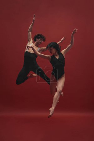 Foto de Joven hombre y mujer, bailarines de ballet en paños negros bailando, actuando sobre fondo rojo. Concepto de arte clásico, estética, emociones, danza de ballet, talento, belleza - Imagen libre de derechos