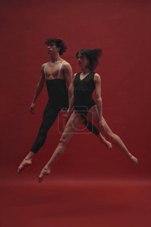 Photo for Young man and woman, ballet dancers in black cloths dancing, performing against red background. Concept of classic art, aesthetics, emotions, ballet dance, talent, beauty - Royalty Free Image