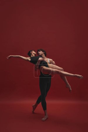 Foto de Mujer joven hermosa y elegante y hombre guapo, bailarina de ballet bailando sobre fondo rojo. Negro y rojo. Concepto de arte clásico, estética, emociones, danza de ballet, talento - Imagen libre de derechos