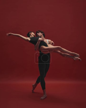 Téléchargez les photos : Belle et élégante jeune femme et bel homme, danseuse de ballet dansant sur fond rouge. Noir et rouge. Concept d'art classique, esthétique, émotions, danse de ballet, talent - en image libre de droit