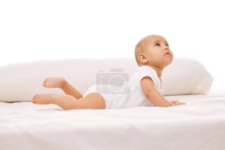 Photo for Playful, active smart child, little baby girl lying on bed and looking upwards, showing curiosity and attention against white background. Concept of childhood, family, care, motherhood, infancy, heath - Royalty Free Image