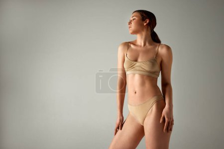 Photo for Beautiful young woman with ponytail, slim, fit body posing in underwear against grey studio background. Self-love and care. Concept of body and health care, female beauty, wellness - Royalty Free Image