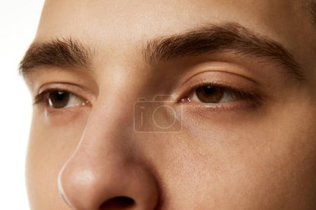 Photo for Close-up of males face focusing on his eyes, eyebrows, and bridge of his nose against white studio background. Model with well kept skin. Concept of beauty treatment, male health, body care, hygiene. - Royalty Free Image
