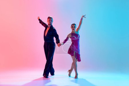 Foto de Hermoso hombre joven y mujer guapa, bailarines de salón haciendo actuación, bailando contra el degradado fondo azul rosado en luz de neón. Concepto de clase de baile, hobby, arte, escuela de baile, talento - Imagen libre de derechos