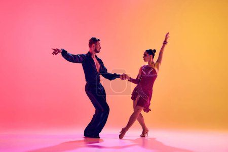 Foto de Bailarinas masculinas y femeninas realizando una danza latina con ropa elegante contra el degradado fondo amarillo rosado en luz de neón. Concepto de clase de baile, hobby, arte, escuela de baile, talento - Imagen libre de derechos