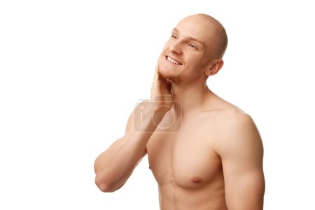 Photo for Handsome bald man with muscular body, unshaved face. standing shirtless, smiling isolated against white studio background. Concept of skin care, male beauty and cosmetics, youth, spa, self-care - Royalty Free Image