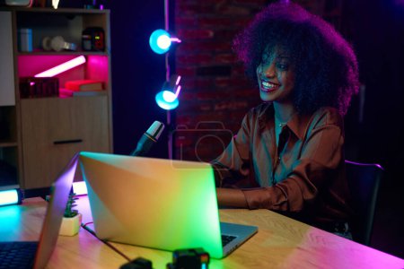 Foto de Joven mujer africana sonriente, influyente en las redes sociales, bloguera sentada con micrófono y grabando una entrevista en podcast. Concepto de comunicación en línea, tecnología moderna, medios de comunicación - Imagen libre de derechos