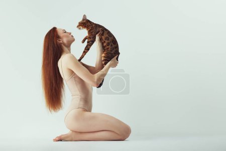 Photo for Bond between human and pet. Beautiful young redhead woman with Bengal cat against white studio background. Concept of animal theme, female beauty, pet care, companion - Royalty Free Image