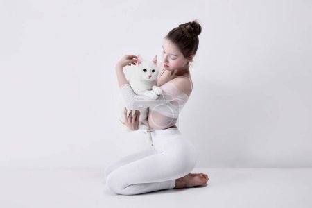 Téléchargez les photos : Connecté à l'animal, lié à des amis animaux de compagnie. tendre jeune fille en vêtements blancs tenant chat blanc sur fond de studio blanc. Concept d'amour, soin des animaux, bien-être - en image libre de droit