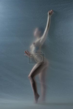 Téléchargez les photos : Silhouette d'élégante jeune femme au corps mince et nu posant nue contre du verre mat transparent. Liberté et autosoin. Concept d'esthétique corporelle, féminité, beauté, santé, art - en image libre de droit