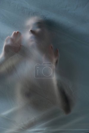 Photo for Silhouette of young woman posing naked with transparent, matte, textured material against grey background. Concept of body aesthetics, femininity, beauty, health, art - Royalty Free Image