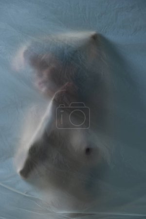 Téléchargez les photos : Silhouette de jeune femme posant nue avec un matériau transparent, mat et texturé sur fond gris. Concept d'esthétique corporelle, féminité, beauté, santé, art - en image libre de droit