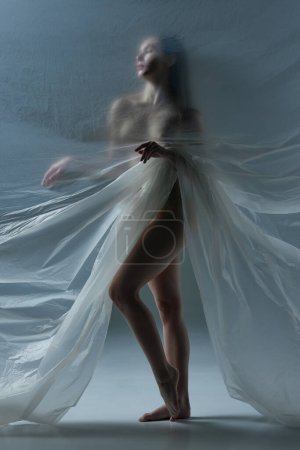 Téléchargez les photos : Silhouette pleine longueur de jeune femme posant nue avec un matériau transparent, mat et texturé sur fond gris. Concept d'esthétique corporelle, féminité, beauté, santé, art - en image libre de droit