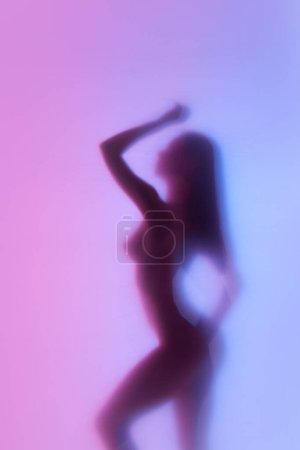 Téléchargez les photos : Silhouette floue d'une femme élégante au corps mince et ajusté posant nue sur fond de dégradé néon. Liberté et amour-propre. Concept d'esthétique corporelle, féminité, beauté, santé, art - en image libre de droit