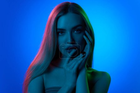 Photo for Elegance. Portrait of young beautiful woman with blonde hair and perfect smooth skin against blue studio background in neon light. Concept of natural beauty, cosmetology, cosmetics, skin care - Royalty Free Image