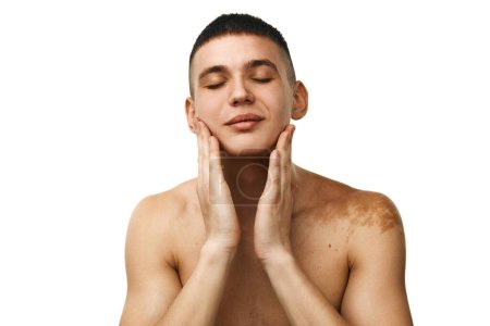 Téléchargez les photos : Jeune homme beau debout torse nu, prenant soin de la peau, lavant le visage isolé sur fond de studio blanc. Concept de beauté masculine, soins de la peau et du corps, hygiène, cosmétiques masculins - en image libre de droit