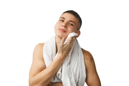 Téléchargez les photos : Beau jeune homme debout torse nu avec serviette sur les épaules, essuyant le visage après avoir lavé isolé sur fond de studio blanc. Concept de beauté masculine, soins de la peau et du corps, hygiène, cosmétiques masculins - en image libre de droit