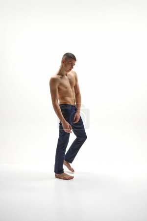 Photo for Full-length image of handsome young shirtless guy with muscular, relief body shape posing in jeans isolated over white studio background. Concept of sportive lifestyle, body and heath care, youth - Royalty Free Image