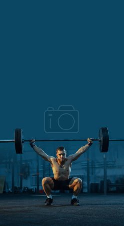 Photo for Shirtless young man with muscular body training in gym, doing squats with heavy barbell in gym. Fitness, sport, workout, power, bodybuilding concept. Banner. Flyer, poster. Empty space to insert text - Royalty Free Image