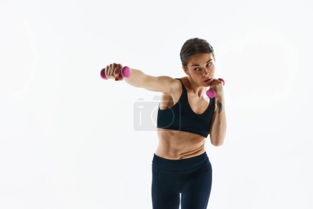 Foto de Mujer joven con entrenamiento muscular, haciendo ejercicios con pesas aisladas sobre fondo blanco del estudio. Concepto de deporte, salud y cuidado del cuerpo, aplicación de fitness, plantillas de ejercicios - Imagen libre de derechos
