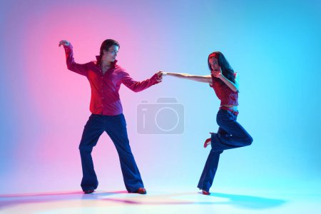 Young stylish people, man and woman dancing retro dance against gradient pink blue background in neon light. Concept of hobby, dance class, party, 50s, 60s culture, youth
