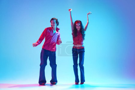 Rock "n" Roll-Ära. Elegantes stylisches junges Paar tanzt Retro-Tanz vor blauem Hintergrund in Neonlicht. Vintage Ästhetik. Konzept von Hobby, Tanzkurs, Party, Kultur der 50er, 60er Jahre, Jugend