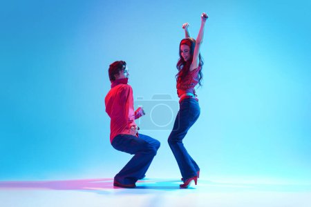 Era de Rockability. Estética de danza retro. Joven elegante hombre y mujer bailando sobre fondo azul en luz de neón. Concepto de pasatiempo, clase de baile, fiesta, 50, cultura de los 60, juventud