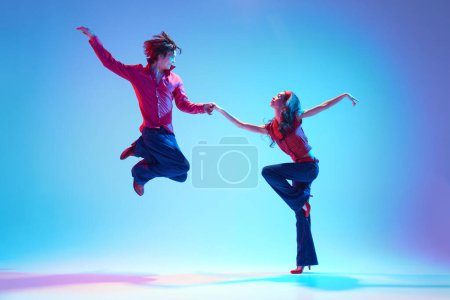 Élégant beau jeune homme et belle femme dansant rock and roll danse rétro sur fond bleu au néon. Concept de passe-temps, cours de danse, fête, années 50, 60 culture, jeunesse
