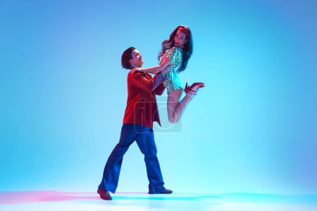 Photo for Poster for retro dance festival. Young stylish man and woman dancing retro dance against blue background in neon light. Concept of hobby, dance class, party, 50s, 60s culture, youth - Royalty Free Image