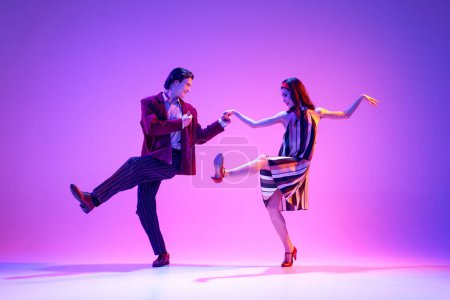 Photo for Young man and woman in stylish clothes dancing retro dance, boogie woogie against purple background in neon light. Concept of hobby, dance class, party, 50s, 60s culture, youth - Royalty Free Image