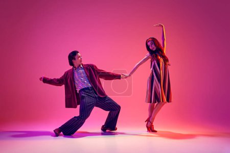 Photo for Artistic young man and elegant woman, couple dancing retro dance in stylish costumes against pink background in neon light. Concept of hobby, dance class, party, 50s, 60s culture, youth - Royalty Free Image