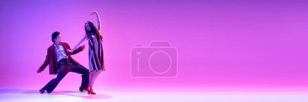 Retro dance aesthetics. Elegant young man and woman dancing against purple background in neon. Concept of hobby, dance class, party, 50s, 60s culture, youth. Banner. Empty space to insert text ad