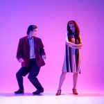 Artistic, talented, positive young man and woman, stylish couple dancing retro dance, boogie woogie against purple background in neon. Concept of hobby, dance class, party, 50s, 60s culture, youth