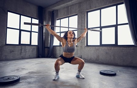 Portrait dynamique de la jeune fille athlétique en tenue de sport travaillant avec haltère en mouvement dans la salle de gym. Force et puissance. Concept de sport professionnel, mode de vie actif, musculation. Publicité
