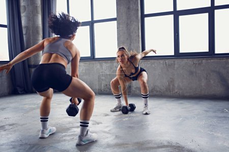 Workout female partners doing squat routine with barbell in motion, action showing strength and balance. Concept of professional sport, active lifestyle, bodybuilding, motivation, energy. Ad
