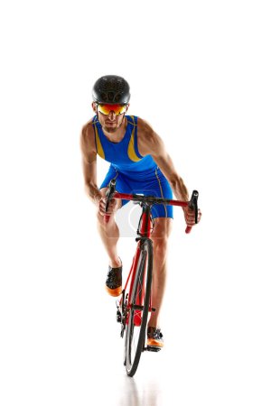 Téléchargez les photos : Image de face de l'homme, athlète en bleu casque de sport et lunettes d'entraînement en mouvement sur vélo isolé sur fond de studio blanc. Concept de sport, mode de vie actif et sain, vitesse, endurance - en image libre de droit