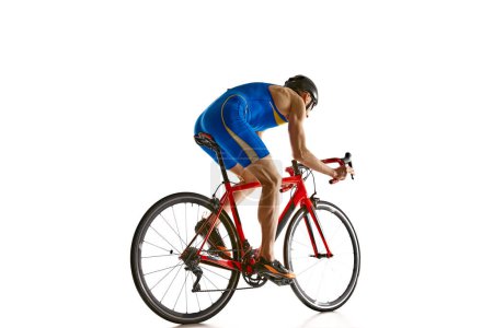 Téléchargez les photos : Image latérale d'un sportif concentré en tenue de sport bleue et casque en mouvement sur un vélo isolé sur fond de studio blanc. Concept de sport, mode de vie actif et sain, vitesse, endurance, passe-temps - en image libre de droit