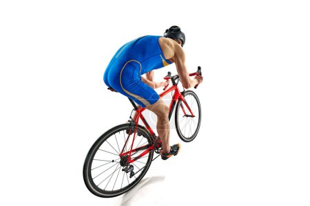 Téléchargez les photos : Vue arrière de l'image d'un sportif concentré en tenue de sport bleue et casque en mouvement sur un vélo isolé sur fond de studio blanc. Concept de sport, mode de vie actif et sain, vitesse, endurance, passe-temps - en image libre de droit