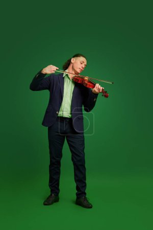 Photo for Talented, artistic man in a suit playing violin against blue background. Classical music live performance. Concept of music, performance, art, entertainment, festival, performance, ad - Royalty Free Image