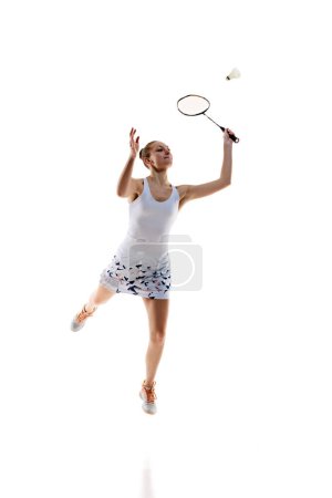 Photo for Concentrated young girl, athlete in motion with racket, playing badminton isolated over white background. Training. Concept of professional sport, active lifestyle, hobby, game - Royalty Free Image