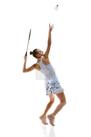 Foto de Vista lateral de la joven deportiva, jugador de bádminton en movimiento sirviendo Shuttlecock con raqueta aislada sobre fondo blanco. Concepto de deporte profesional, estilo de vida activo, hobby, juego - Imagen libre de derechos