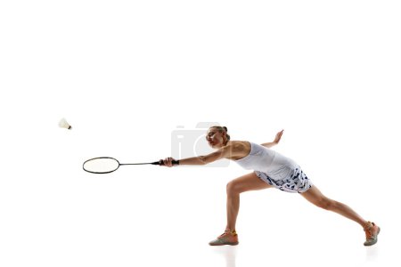 Téléchargez les photos : Jeune fille concentrée, athlète en mouvement avec raquette, jouant au badminton, frappant le volant isolé sur fond blanc. Concept de sport professionnel, mode de vie actif, passe-temps, jeu - en image libre de droit