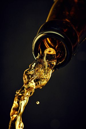 Téléchargez les photos : Gros plan de la bouteille de bière avec bière fraîche lager coulant sur fond sombre. Boisson dorée avec bulles. Concept de boissons alcoolisées et non alcoolisées, rafraîchissements. Affiche, bannière pour la publicité - en image libre de droit