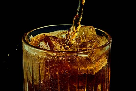 Foto de Soda, coca cola, cerveza oscura vertiendo de botella en vaso con cubitos de hielo sobre fondo negro. Concepto de bebidas alcohólicas y no alcohólicas, refresco. Póster, banner para anuncio - Imagen libre de derechos