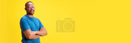 Photo for Confident, smiling African-American man standing with hands crossed against yellow studio background. Success. Concept of human emotions, casual fashion, lifestyle. Banner. Empty space for text, ad - Royalty Free Image