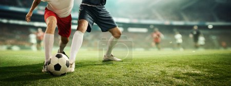Téléchargez les photos : Image dynamique des jambes masculines, des joueurs de football en mouvement sur une balle dribblante classée, jouant au football au modèle de stade 3D avec fond flou. Concept de sport professionnel, compétition, tournoi - en image libre de droit