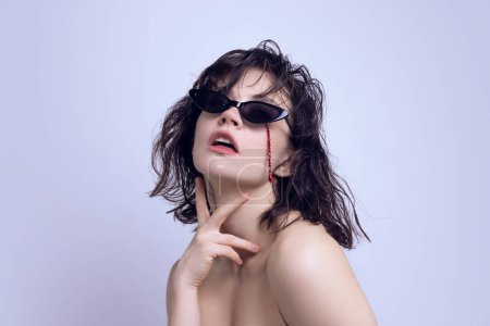 Beautiful young woman with wet hair wearing sunglasses, red beads draped over face. Emerging fashion trends. Concept of modern beauty standards, plastic surgery, health, cosmetology