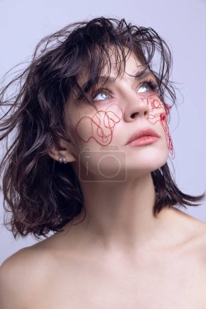 Beautiful young woman with tangled red strings on face, messy hair, looking upwards. Modern interpretations of beauty. Concept of modern beauty standards, plastic surgery, health, cosmetology